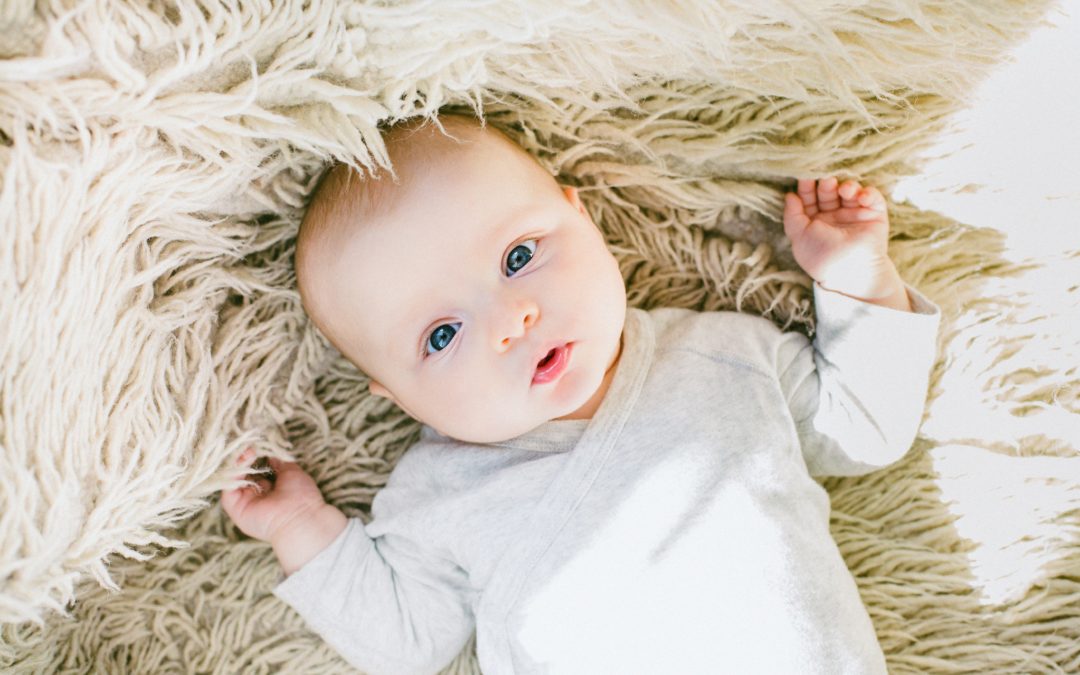 baby with blue eyes laying on white rug